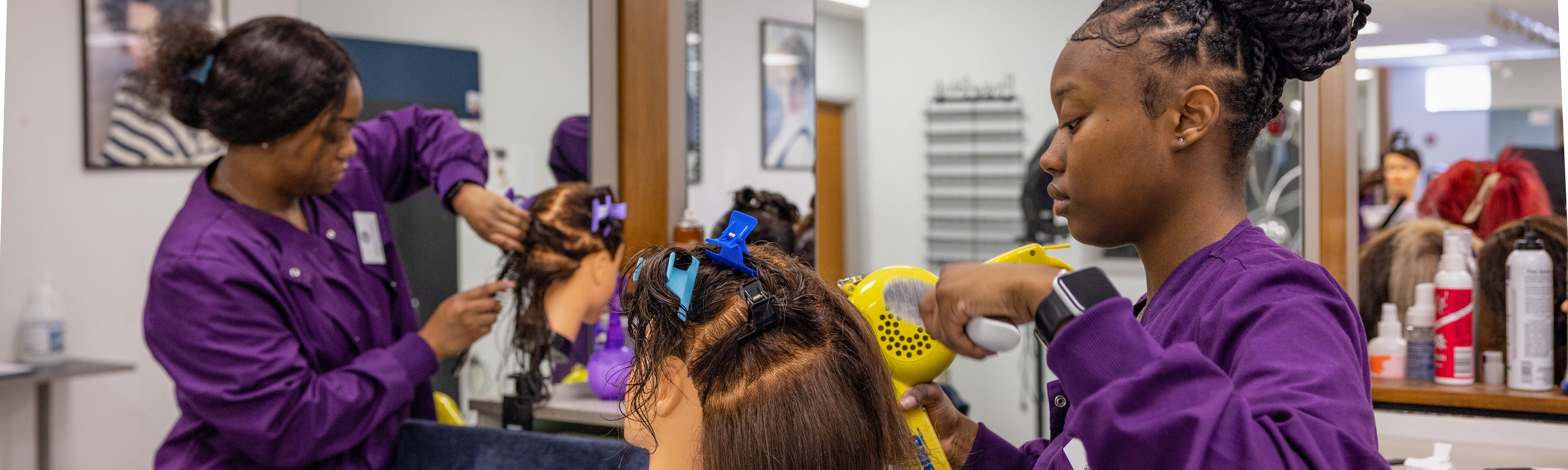 A Cosmetology student styles hair on a mannequin head.