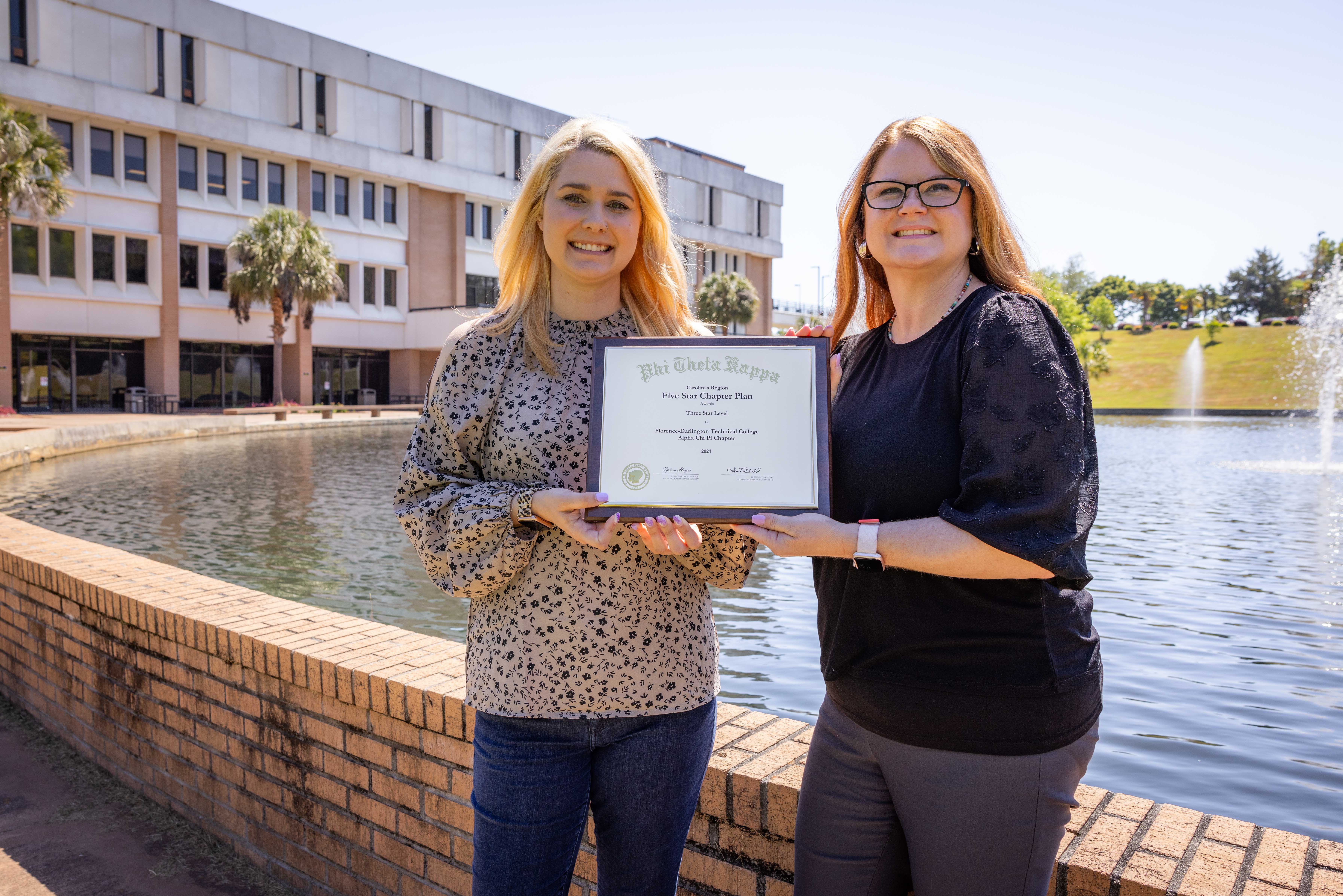 PTK Advisors Hannah Harpe and April Cudd hold a plaque for their awards in front of the FDTC 5000 building.