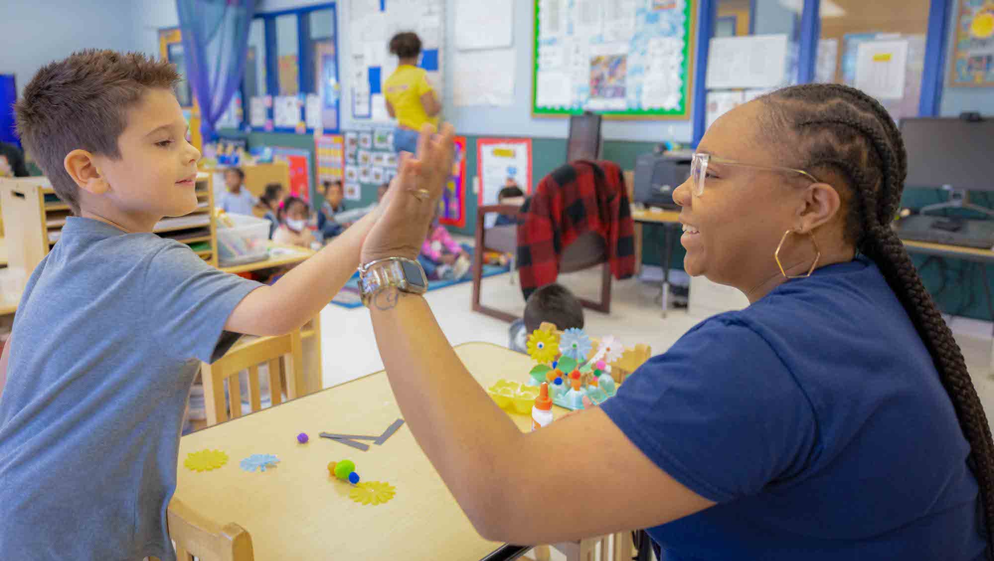 An Early Childhood Education student claps hands with a young child in the ECE building.