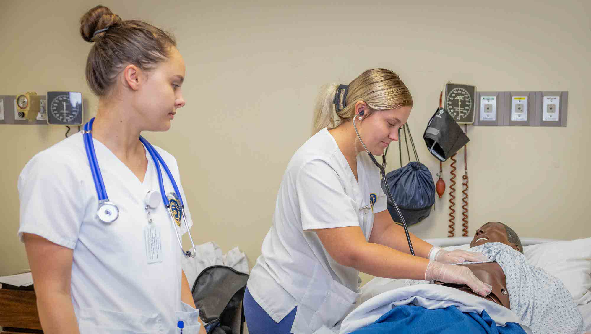 Two nursing students practicing technique on a training dummy.