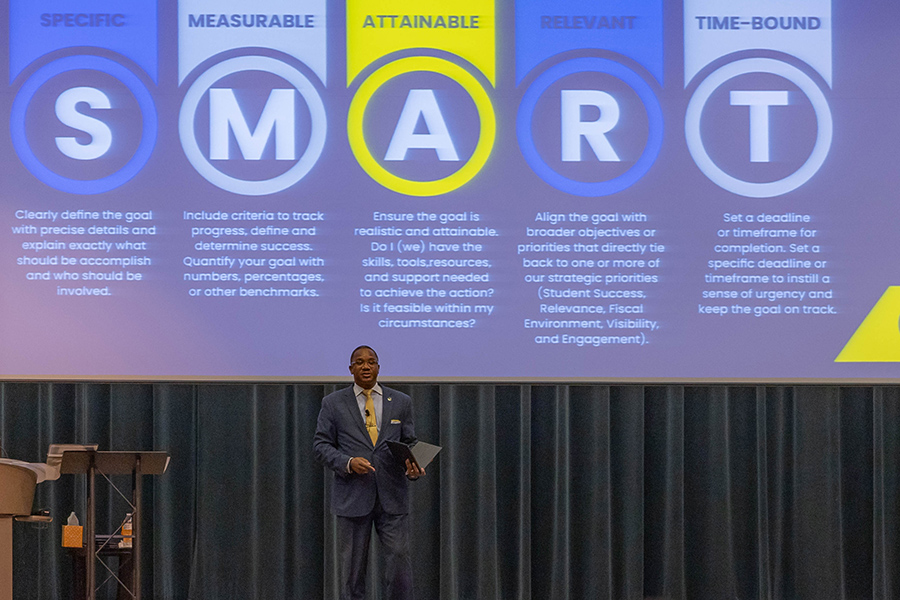 Dr. Jermaine Ford is seen speaking to a group of people while standing in front of a large screen with an image on it.